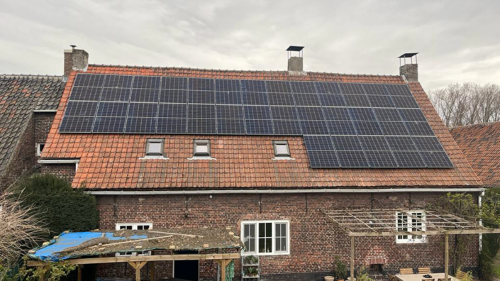 Grote installatie van zonnepanelen op een hellend dak met oranje dakpannen van een landelijke woning, drie dakvensters zichtbaar