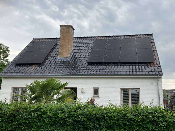 Witte woning met zwarte zonnepanelen op beide zijden van het dak, donkere dakpannen en een grote schoorsteen in het midden