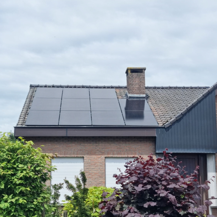 Laag hellend dak met zwarte zonnepanelen, schoorsteen in het midden en groene tuin op de voorgrond