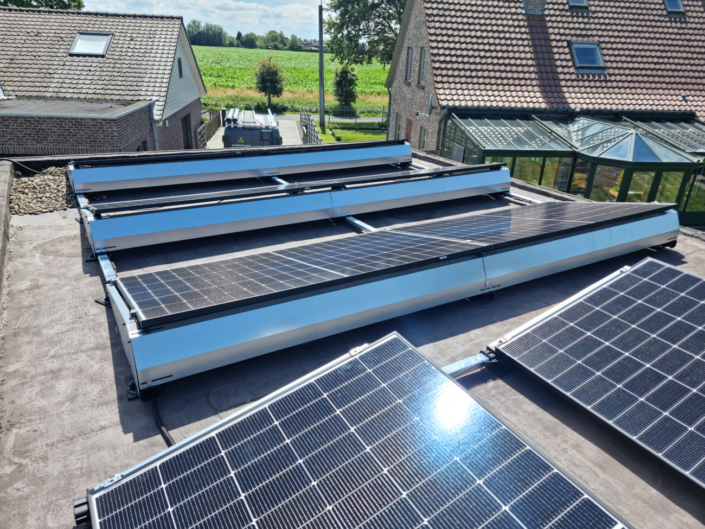 Installatie op plat dak met dubbele rijen zonnepanelen in oost-west configuratie, landelijke omgeving op de achtergrond