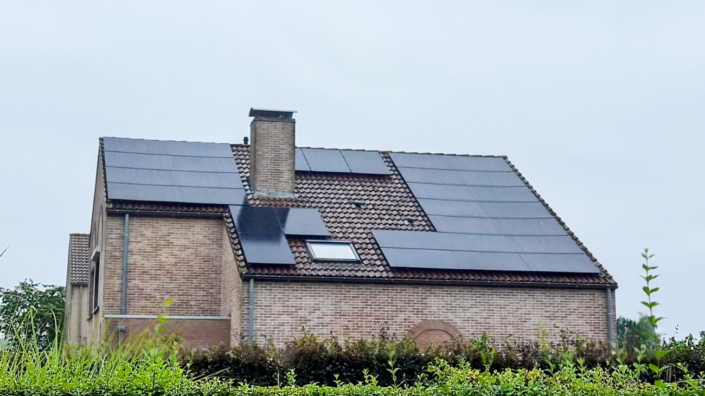 Vrijstaande woning met zonnepanelen verspreid over drie dakvlakken rond een schoorsteen, rode dakpannen en zicht op tuin