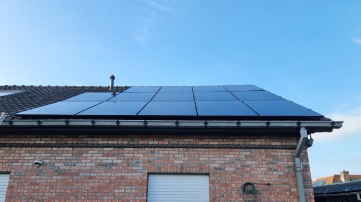 Zwarte zonnepanelen op hellend dak van aanbouw, rode gevelsteen, strakke afwerking met zicht op blauwe hemel