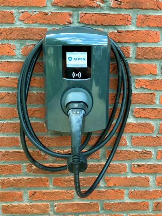 Compacte Alfen laadpaal aan rode bakstenen gevel in Eeklo met aangesloten laadkabel voor elektrische wagen