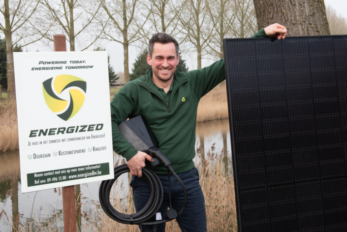Michiel glimlachend met een zonnepaneel en een laadpaal in zijn handen