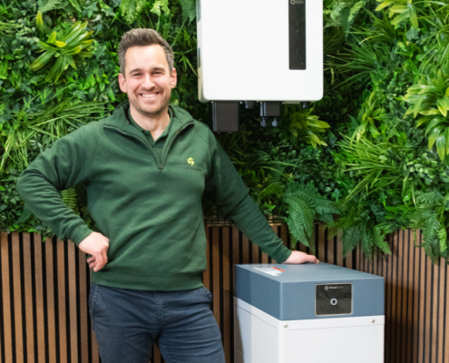 Michiel staat bij een thuisbatterij Michiel toont de grote van een thuisbatterij en hoe het eruit ziet geplaatst bij je thuis.