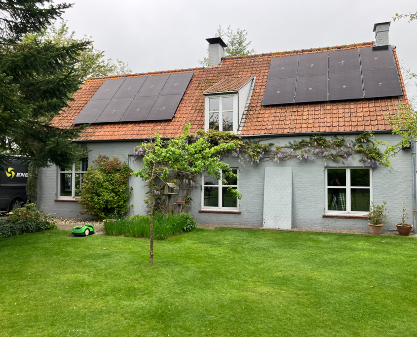 Zonnepanelen op oranje dakpannen van landelijke woning met blauwe ramen en veel groen